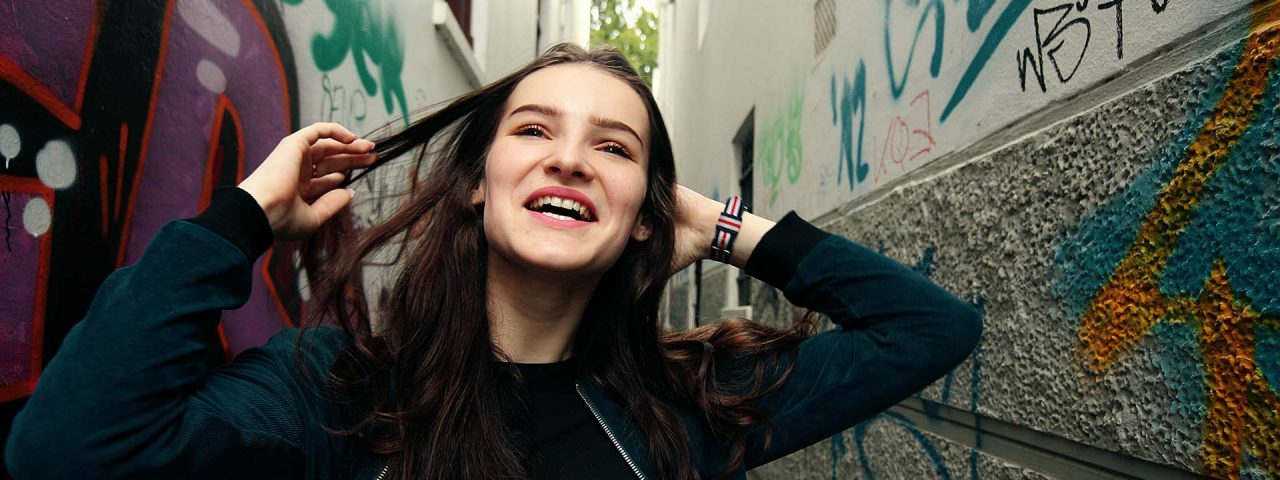 Young person smiling in allay with graffiti on walls behind