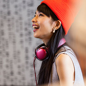 Person wearing beanie smiling skywards wearing earphones.