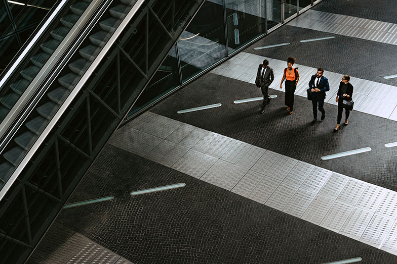 4 people walking towards escalator 