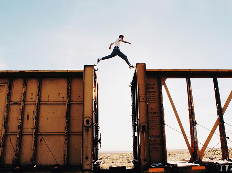 A person jumping between the tops of two cargo train carriages