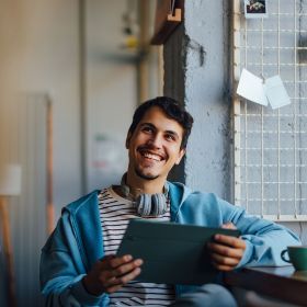 Happy younge person using a tablet whilst sitting at desk in industrial setting