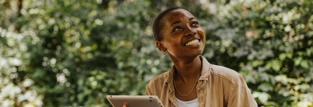 smiling young person holding tablet in forest